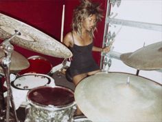 a woman is playing drums in front of a drum set and red wall behind her