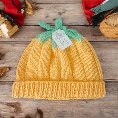 a yellow knitted hat with a green bow sits on a wooden table next to other items