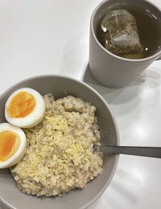 two boiled eggs sit on top of rice in a bowl next to a cup of tea