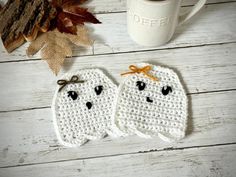 two crocheted ghost mug cozyies next to a coffee cup and autumn leaves