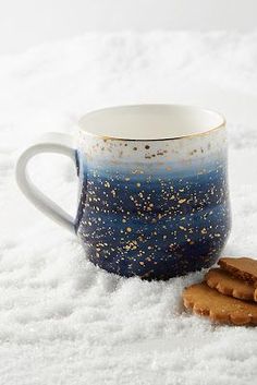 a cookie and coffee mug sitting in the snow with some cookies on it's side