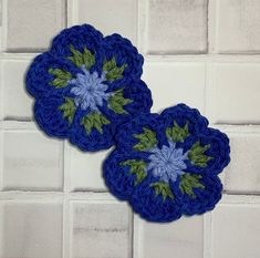 two blue crocheted coasters sitting on top of a white tile wall next to each other