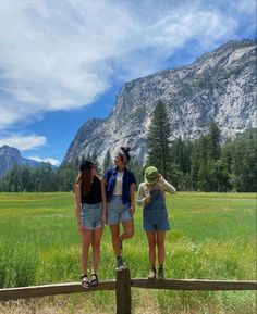 three girls standing on a fence looking up at the mountains