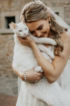 a woman in a wedding dress holding a white cat on her chest and smiling at the camera