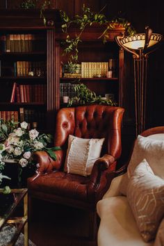 a brown chair sitting in front of a book shelf filled with lots of books and flowers