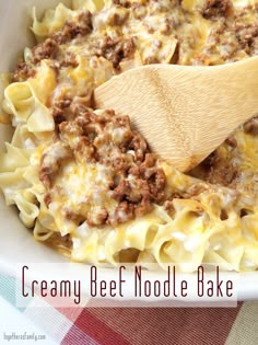 a wooden spoon in a bowl filled with creamy beef noodle bake and cheese