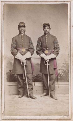 two men in uniforms standing side by side with canes and hats on their heads