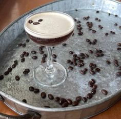 a drink in a glass sitting on top of a metal tray filled with coffee beans