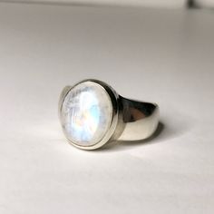 "Pictured here is a vibrant moonstone ring that weighs 8.2 grams and is US size 7 1/4. It is framed in sterling silver. This ancient gem, moonstone, has been admired for centuries. It was thought that moonstone was created from rays of the moon which provided a feeling of mystery and magic for those who held it. Moonstone is thought of as the \"'lovers' stone\" which evokes tender feelings and safeguarding the true joys of love. Some believe that wearing this stone strengthens our intuition and Modern Oval Sterling Silver Moonstone Ring, Modern Oval Moonstone Ring With Large Stone, Sterling Silver Oval Rings With Moon Phase, Sterling Silver Oval Rings With Moon Phase Detail, Silver Oval Moon Phase Ring, Modern Silver Moonstone Cabochon Ring, White Polished Moonstone Ring, Silver Oval Ring With Moon Phase, Silver Oval Rings With Moon Phase