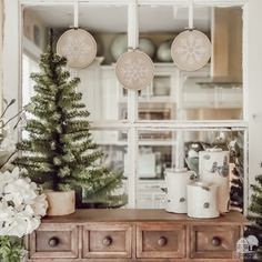 three christmas trees sitting on top of a wooden dresser in front of a glass window