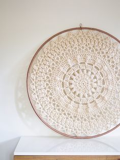 a crocheted doily hanging on the wall above a white table with a wooden drawer