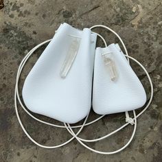 two white purses sitting on top of a stone floor next to a corded charger