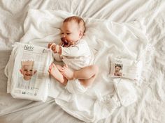 a baby laying on top of a bed next to a pillow and some diapers