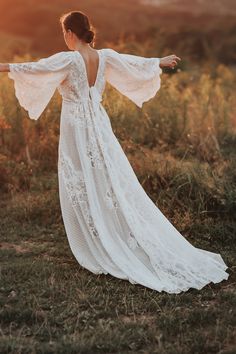 a woman in a long white dress is standing in the grass with her arms outstretched