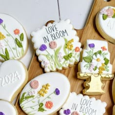 decorated cookies on a wooden cutting board with flowers and love in bloom written on them