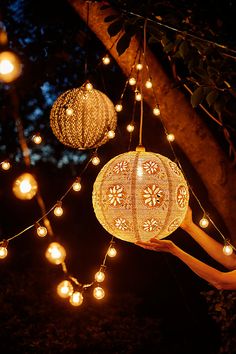 a woman is holding a lantern in her hand and some lights are hanging from the tree