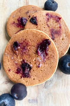 three pancakes with blueberries are on a wooden table