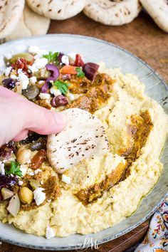 a plate with mashed potatoes, olives and feta cheese being served to someone