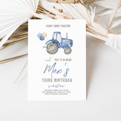 a blue tractor birthday party card with balloons and palm fronds on the table