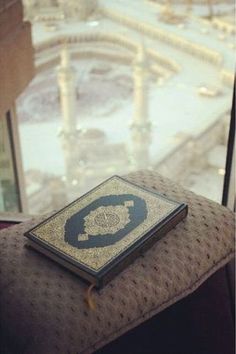 an open book sitting on top of a brown ottoman in front of a glass window