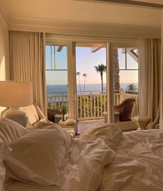 a bed with white sheets and pillows in front of a large window overlooking the ocean