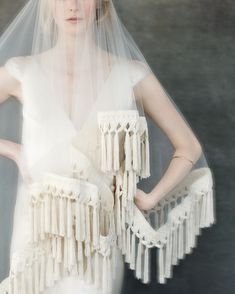 a woman in a white wedding dress with a veil on her head and fringes around her shoulders