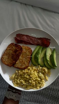 a white plate topped with eggs, bacon and avocado on top of a bed