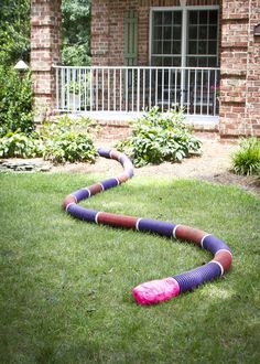 a colorful snake made out of plastic tubes in the grass next to a brick house