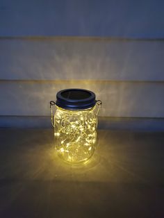 a mason jar filled with fairy lights sitting on top of a wooden table next to a wall