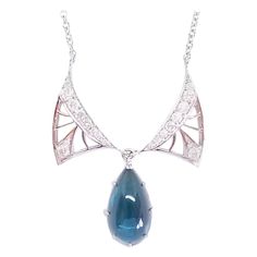 This Custom Designed and Crafted, One of a Kind Drop Necklace by Artisan Tom Castor features in Art Nouveau Tradition, Delicate and Open, Diamond Wings. Framed by the Wings is a Natural Indicolite Blue Tourmaline of 7.55 Carats in weight and a measurement of 10mm Wide x 18.5mm Long and a High Cabochon Depth of 5mm. The Gem is of AAA Quality and is held in an 18 Karat White Gold backed frame and prongs. The Drop and Wings are hinged for proper movement and placement on the Décolletage. The Diamon Formal Teardrop Cabochon Necklace, Luxury Pear-shaped Necklaces With Polished Finish, Luxury Pear-shaped Polished Finish Necklaces, Luxury Pear-shaped Necklace With Polished Finish, Luxury Pear-shaped Polished Finish Necklace, Diamond Cabochon Pendant Necklace, Elegant Wing-shaped Yellow Gold Necklace, Luxury Diamond Necklace For Collectors, Elegant Yellow Gold Wing-shaped Necklace