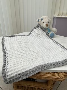 a crocheted blanket on top of a wicker basket with a teddy bear