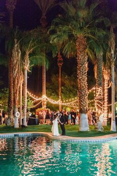 a bride and groom standing in front of a pool surrounded by palm trees at night