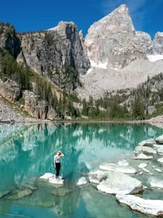 a person standing on rocks in front of a mountain lake with blue water and ice floes