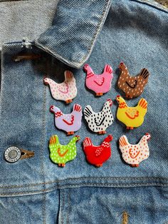 several different colored chicken pins sitting on top of a jean jacket with holes in the back