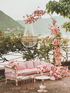 an outdoor seating area with pink flowers on the table and in the background there is a chandelier