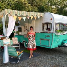 a woman standing in front of an old camper trailer with awnings on the side