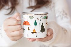 a woman holding a coffee mug with camping designs on it