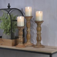 three candles are sitting on a shelf next to a potted plant and birdcage