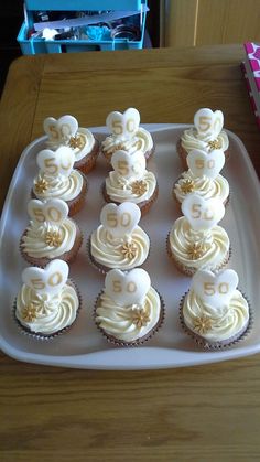 cupcakes with white frosting and gold decorations on a tray in front of a wooden table