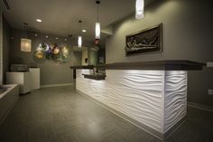 an empty reception area with white counter tops and wood flooring, along with lights hanging from the ceiling