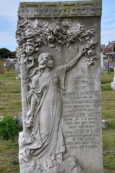 a statue with flowers on it in the middle of a cemetery area, surrounded by tombstones