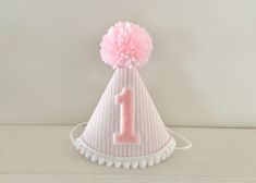 "NEW and even cuter in person...if that's possible! A small party hat made of stiffened felt with light pink seersucker fabric, with a pink #1, and trimmed with mini white pom poms on bottom and a light pink/white yarn pom pom on the top. Attached to a 1/8\" elastic- to be worn comfortably like a headband. SIZE OPTIONS: MINI: $17.95 3\" x 4.25\" photos 4 SMALL:$19.95 4\"x5.25\" photo 1,2 and 3 shows size on 1 year old *I customize cake toppers and banners to match too! Message me! * Can be made White Hats For First Birthday And Spring, White Hat For First Birthday In Spring, White Hats For First Birthday In Spring, Adjustable White Mini Hat For First Birthday, Cute Pink Mini Hat For First Birthday, Playful Pink Mini Hats For Birthdays, Playful Pink Mini Hats For Birthday, Girl Cake Smash, First Birthday Hat