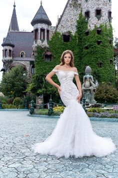 a woman is posing in front of a castle wearing a wedding dress with an off the shoulder neckline