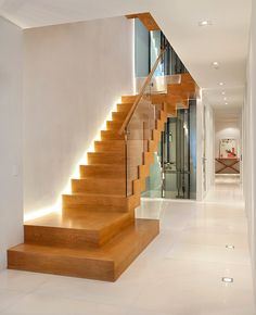 a wooden stair case next to a white wall with lights on the bottom and side