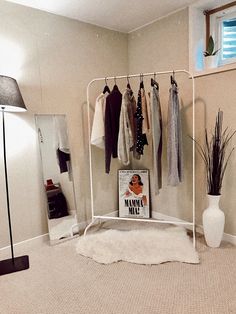 a white rack with clothes hanging on it in a room next to a lamp and mirror