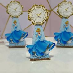 three disney princess figurines are sitting on a table next to each other with clocks in the background