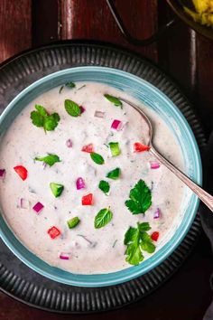 a blue bowl filled with white sauce and garnished with cilantro, red onion, green leaves