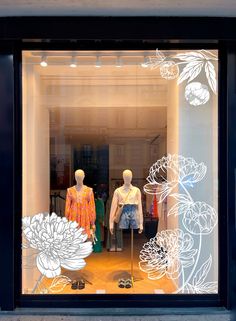 two mannequins in a store window with white flowers on the front and behind them