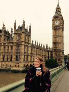 a woman standing on a bridge taking a photo in front of big ben