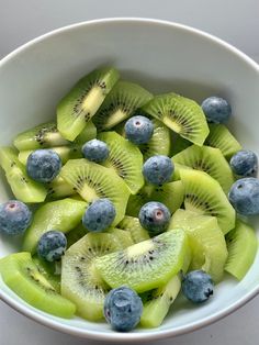 a bowl filled with kiwis and blueberries on top of a white table